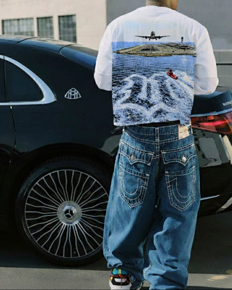 Person wearing a t-shirt with a graphic design standing next to a black car.