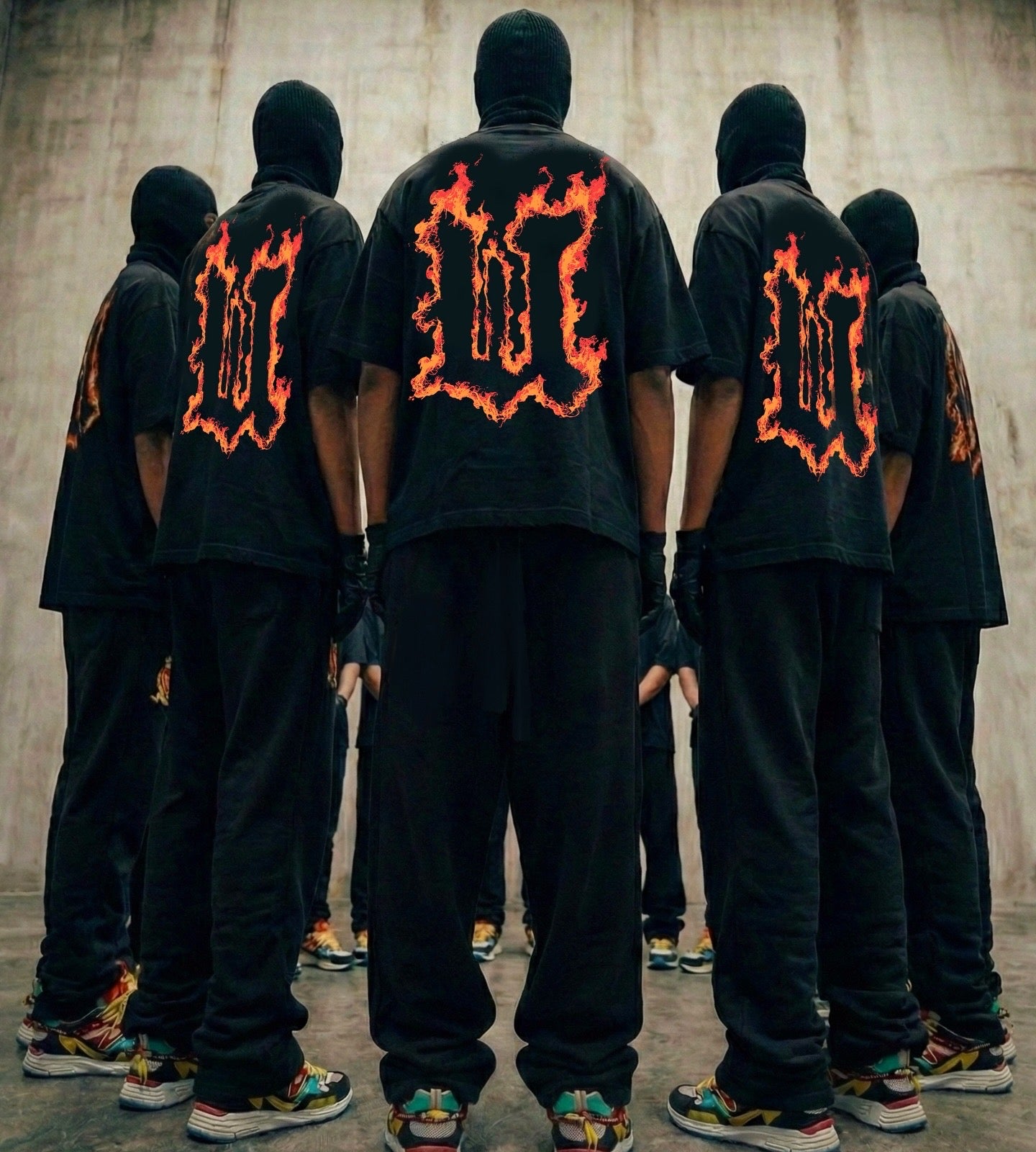 Group of people wearing black outfits with fiery designs on the back against a concrete wall.