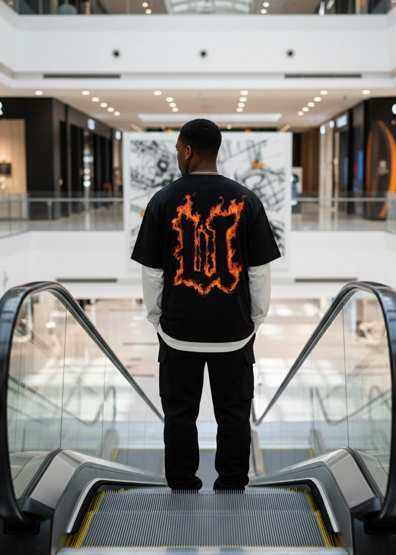 Person wearing a black t-shirt with orange design on an escalator in a mall.